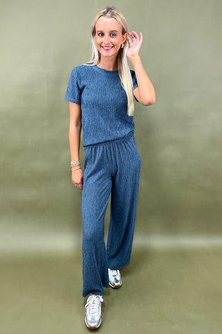 Woman wearing a blue knit outfit with white sneakers against a green background