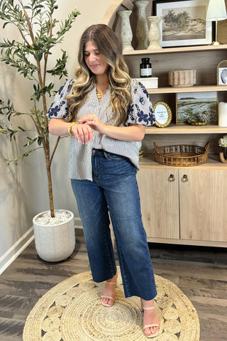 Woman in a floral top and jeans standing in a room with decor elements.