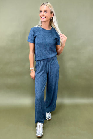 Woman wearing a blue knit outfit with white sneakers on a plain background