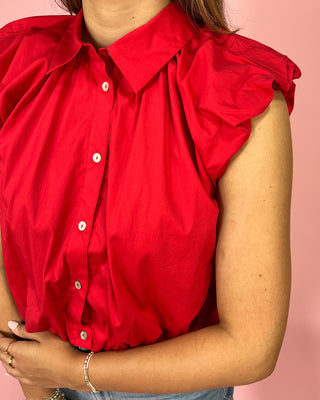 Red sleeveless blouse with ruffled shoulders on a pink background
