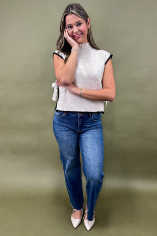 Woman wearing a sleeveless white top and blue jeans against a green background
