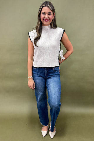 Woman wearing a white sleeveless top and blue jeans against a green background