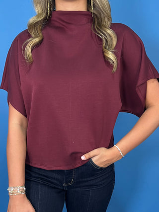 Burgundy mock neck top with relaxed short sleeves and a smooth, polished finish.