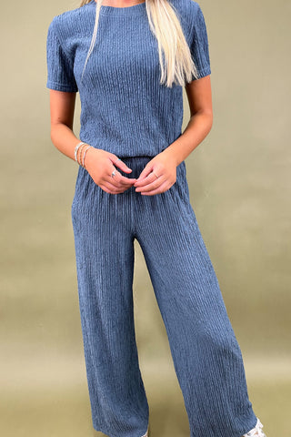 Person wearing a blue ribbed outfit against a beige background