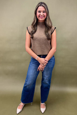 Woman wearing a brown sleeveless top and blue jeans against a green background