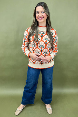 Woman wearing a patterned sweater and blue jeans against a green background