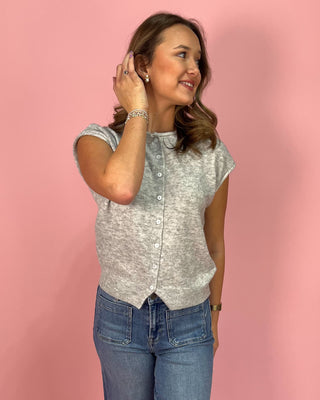 Heather gray sleeveless knit button-front top with subtle cap sleeves and ribbed trim, paired with high-rise wide leg jeans and pointed metallic flats, styled against a pink background.