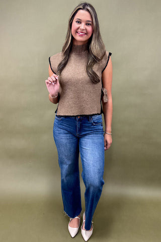 Woman wearing a brown sleeveless top and blue jeans against a beige background