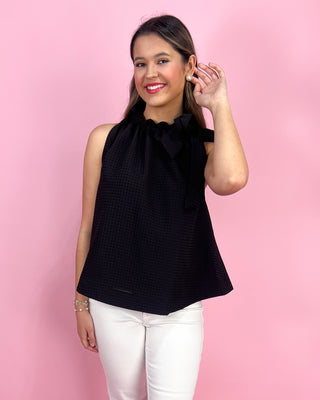 Woman wearing a black sleeveless top with a bow detail against a pink background