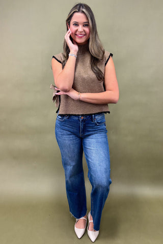 Woman wearing a brown sleeveless top and blue jeans against a green background