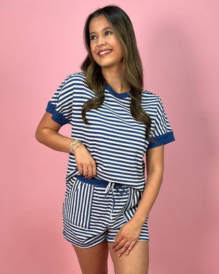 Woman wearing a blue and white striped pajama set against a pink background