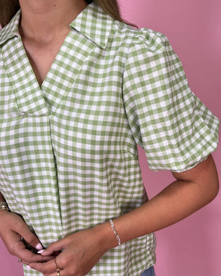 Green and white checkered shirt worn by a person on a pink background