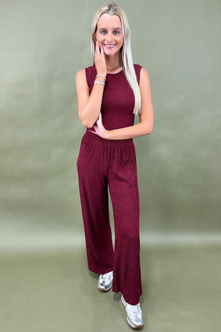 Woman wearing a burgundy jumpsuit against a plain background
