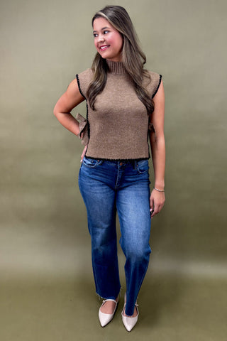 Woman wearing a brown sleeveless top and blue jeans against a green background
