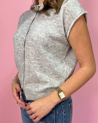 Heather gray sleeveless knit button-front top with subtle cap sleeves and ribbed trim, paired with high-rise wide leg jeans and pointed metallic flats, styled against a pink background.