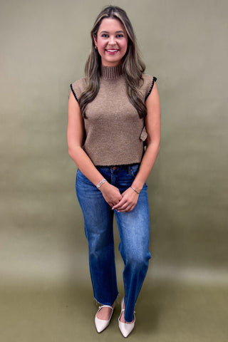 Woman wearing a brown sleeveless top and blue jeans against a plain background