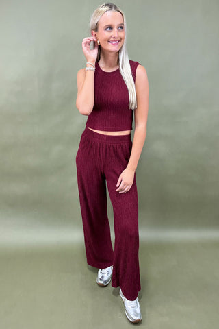 Woman wearing a burgundy outfit with wide-leg pants against a plain background