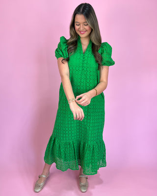 Woman wearing a green dress with ruffled sleeves against a pink background