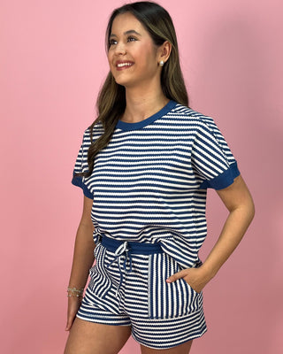 Woman wearing a navy and white striped outfit against a pink background