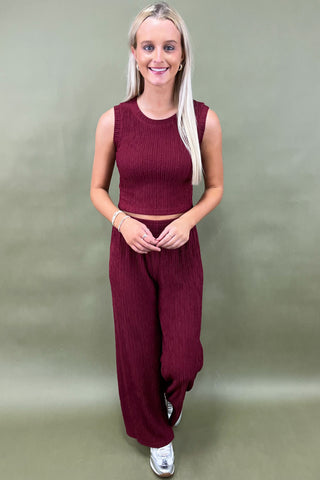Woman wearing a maroon sleeveless top and wide-leg pants against a plain background