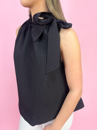 Black sleeveless top with bow detail on a pink background