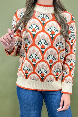 Person wearing a patterned sweater with orange and beige design on a green background
