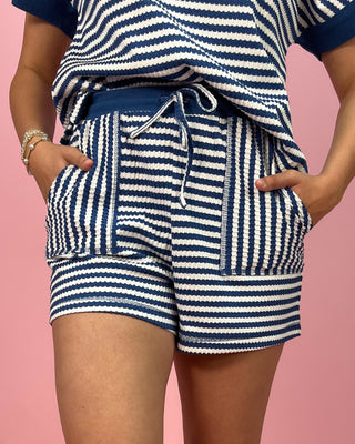 Person wearing blue and white striped shorts with a matching top on a pink background