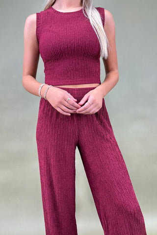 Person wearing a maroon ribbed top and pants on a plain background