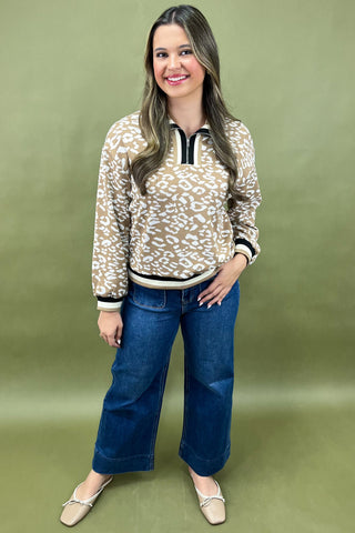 Woman wearing a patterned top and blue jeans against a green background