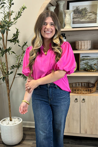 Woman in a pink blouse and blue jeans standing in a room with decor elements.