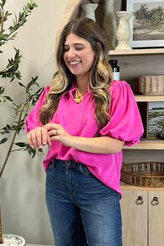 Woman wearing a bright pink blouse and blue jeans standing in a room with decor elements.
