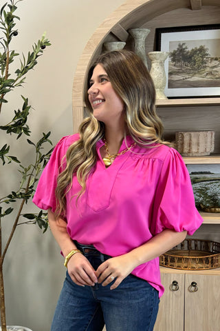 Woman wearing a bright pink blouse and blue jeans standing in a room with decor elements.