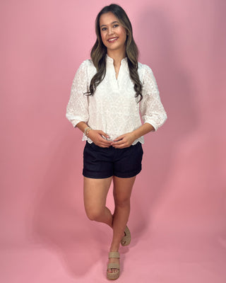 Woman wearing a white blouse and black shorts on a pink background