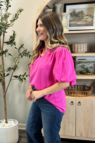 Woman in a bright pink blouse and blue jeans standing in a room with decor elements.