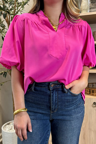 Person wearing a bright pink blouse and blue jeans indoors.