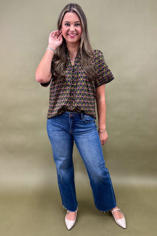 Woman wearing a patterned blouse and blue jeans against a green background