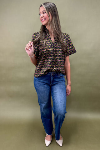 Woman wearing a patterned top and blue jeans against a green background