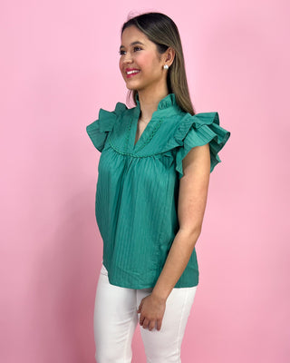 Woman wearing a teal blouse with ruffled sleeves against a pink background