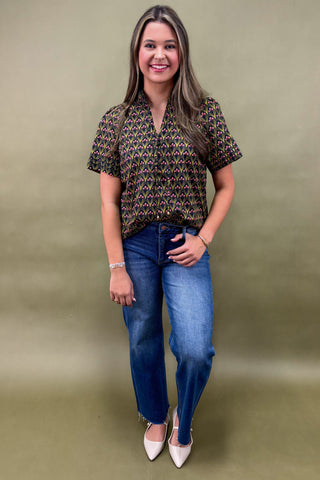 Woman wearing a patterned top and blue jeans against a green background