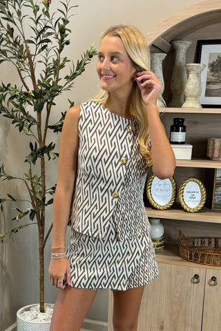Woman in a patterned dress standing in a room with decorative items on a shelf.
