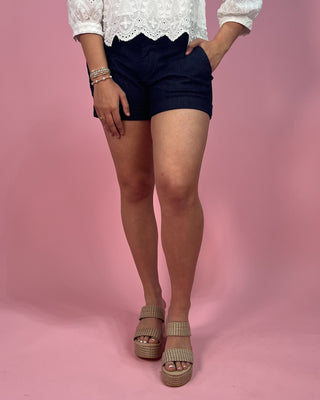 Person wearing navy shorts and a white lace top on a pink background