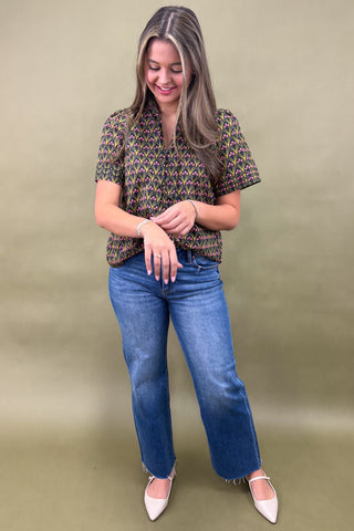 Woman wearing a patterned blouse and blue jeans against a beige background