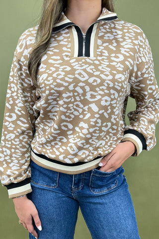 Person wearing a beige leopard print pullover with blue jeans on a green background