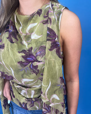 A sleeveless draped top with an olive green base and a purple and white floral print, worn by a model against a solid blue background.