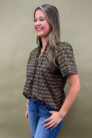 Woman wearing a patterned blouse and jeans against a plain background