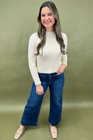 Woman wearing a cream sweater and blue jeans against a green background