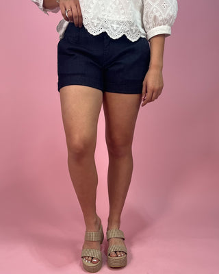 Person wearing navy shorts and a white lace top on a pink background