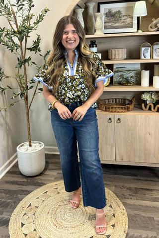 Woman standing in a room with a plant and wooden cabinet in the background