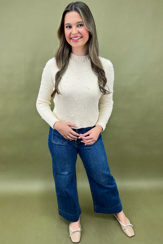 Woman wearing a cream sweater and blue jeans against a green background