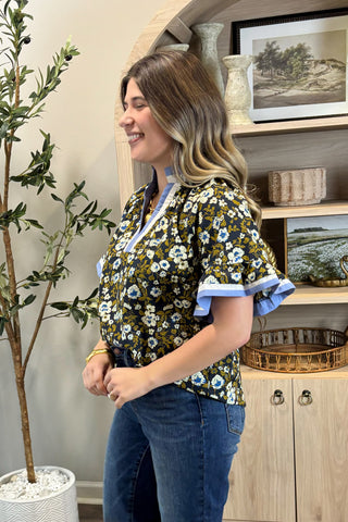 Woman wearing a floral blouse with ruffled sleeves in a home setting.